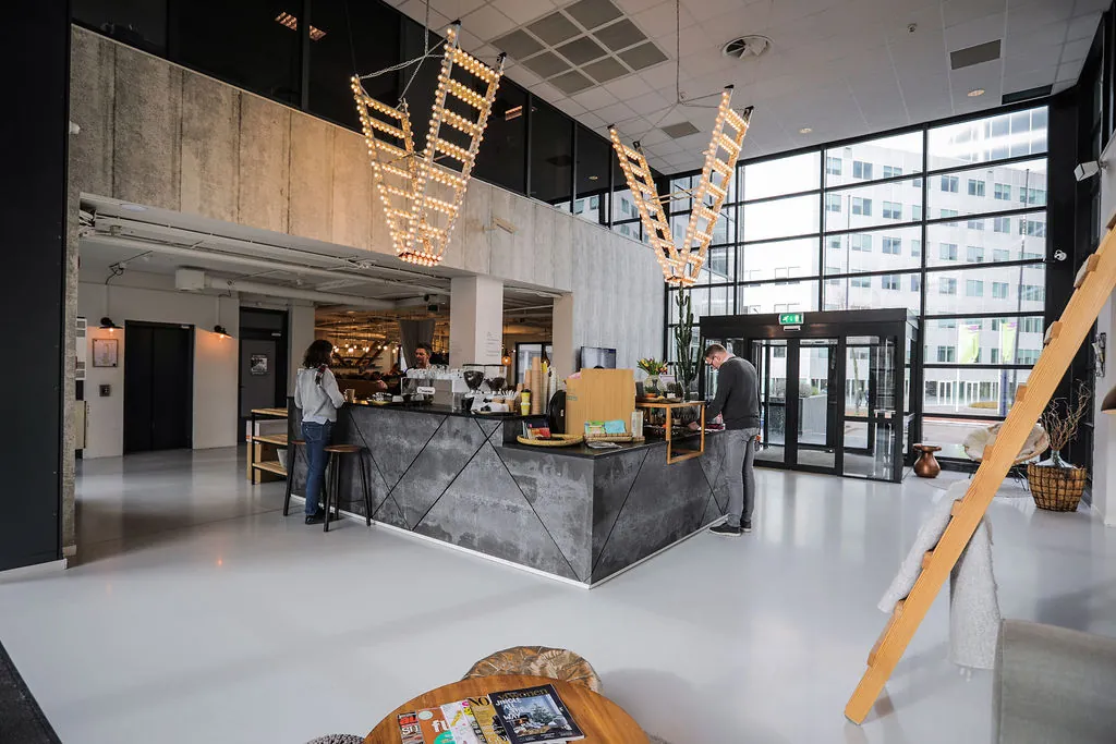 Moderne ontvangsthal met koffiebar aan de Marten Meesweg, met grote ramen en een industriële inrichting.